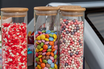 Brightly colored jars filled with assorted candies and sweets are showcased at a lively market, attracting visitors with their vibrant hues and enticing appearance