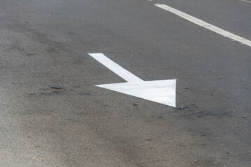 A clear white arrow is marked on the asphalt surface, guiding vehicles to turn left at a busy urban...