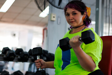Beautiful overweight Latina woman exercising with dumbbells, looking at herself in the mirror at a...