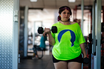 Beautiful overweight Latina woman lifting dumbbells in a gym, wearing a green 80s-style t-shirt,...