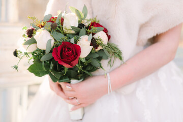 Bridal bouquet featuring red and white roses with greenery held by a bride in a winter setting
