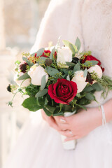 Bridal bouquet of red and white roses with greenery held by a bride in a soft, elegant setting...