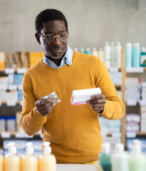 African man choose buy painkiller tablet at pharmacy, compare with other good. Client check for...