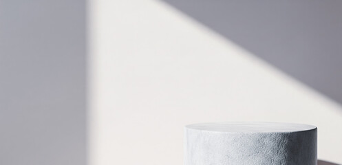Cylinder pedestal against a white wall with a shadow pattern.