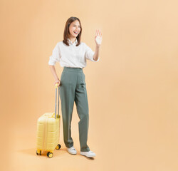 Happy Asian business woman holding suitcase isolated on beige color background, travel concept.