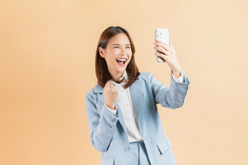 Asian businesswoman holding smartphone with fists clenched celebrating victory expressing success on isolated background.