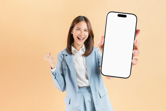 Confident Asian businesswoman holding big smartphone mockup of blank screen and smiling on beige color background.