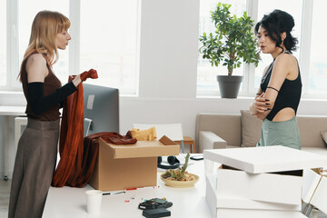 Two young women colleagues from Gen Z socializing and working together in a modern workplace,...
