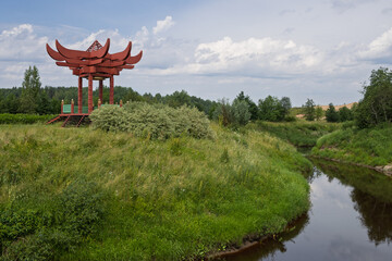 Chinese gazebo on the bank of a small river. Summer view of a decorative wooden gazebo in Chinese style. Tourist attraction. Maryino Estate, Leningrad Region, Russia.