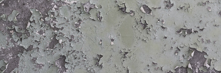 Peeling paint on the wall. Panorama of a concrete wall with old cracked flaking paint. Weathered rough painted surface with patterns of cracks and peeling. Wide panoramic grunge texture for background