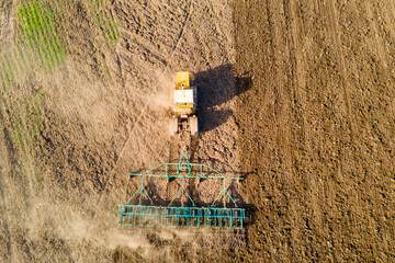 Aerial view of a yellow tractor methodically tilling a brown field. the machine is working efficiently, demonstrating modern agricultural techniques against a backdrop of soil textures.