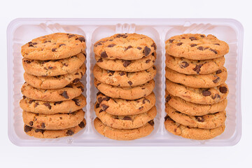 Stacked chocolate chip cookies in a clear plastic tray on a white background. Crunchy golden biscuits perfect for snack, packaging design, bakery display or dessert advertising visuals.