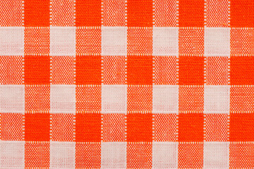 Close-up of orange and white gingham checkered fabric with a rustic woven texture, perfect for picnic tablecloths, farmhouse decor, vintage kitchen style, and cheerful home textile backgrounds.