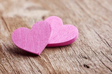Two pink wooden hearts one overlapping the other set against a rustic textured wood surface