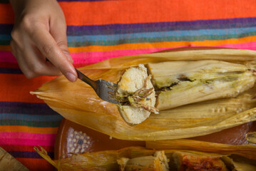 Hands of a person cutting a tamale with a fork. Tamale, typical Mexican food.
