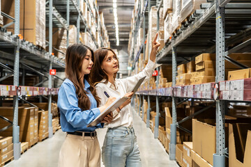 Two young asian women share insights and strategies while inspecting numerous packages and boxes engage in lively discussion while navigating a bustling warehouse filled with packages