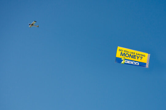 USA: Single engine airplane in clear blue sky towing a bright yellow Geico Insurance banner