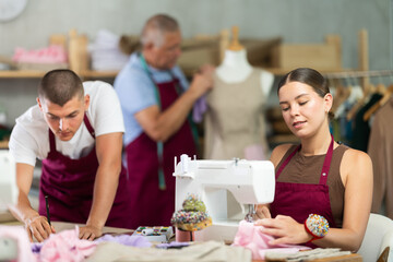 Female seamstress works on a machine at a straw next to a young fashion designer and an elderly...