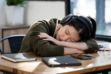 Tired female student with headphone sleeping at desk after hard learning