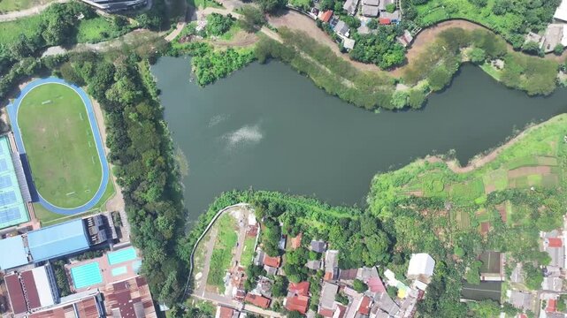 a lake covered in green plants located in the middle of the city and has a flow to the river to dam flooding