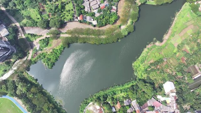 a lake covered in green plants located in the middle of the city and has a flow to the river to dam flooding