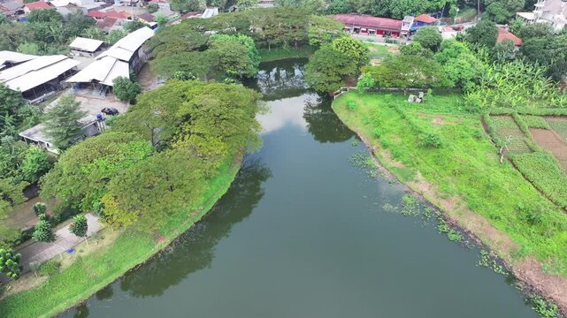 a lake covered in green plants located in the middle of the city and has a flow to the river to dam flooding