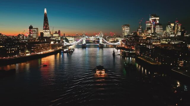 United Kingdom, London: Breathtaking aerial view of London at night, illuminated Tower Bridge, The Shard, and cityscape reflecting on the River Thames with boat, creating mesmerizing urban nightscape