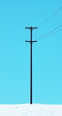 A tall, dark utility pole stands against a bright, vibrant blue sky, reaching from a snow-covered landscape