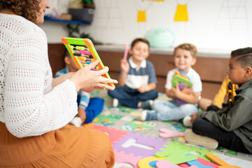 Preschool teacher shows an abacus to a group of attentive children seated on the classroom floor....