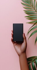 Hand holding a black power bank against a pink background with palm leaves