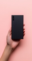 A hand holds a matte black rectangular portable charger against a soft pink background.  The charger is simple and modern