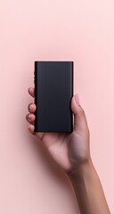 Hand holding a black power bank against a blush-pink background