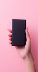 Hand holding a black portable battery pack against a pink background