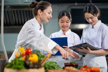 Professional chef is teaching young culinary class student to prepare fresh ingredient for the meal inside the restaurant kitchen for fine dining gourmet and cooking school concept
