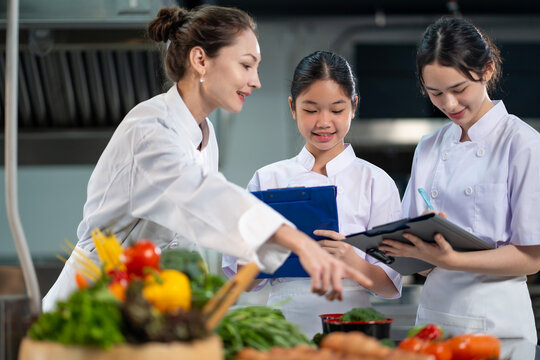 Professional chef is teaching young culinary class student to prepare fresh ingredient for the meal inside the restaurant kitchen for fine dining gourmet and cooking school concept