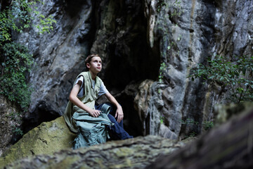 A hiker rests on a mossy rock inside a rocky canyon, surrounded by lush greenery. The peaceful scene captures a moment of solitude, reflection, and connection with nature during an outdoor adventure.