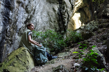 A hiker rests on a mossy rock inside a rocky canyon, surrounded by lush greenery. The peaceful scene captures a moment of solitude, reflection, and connection with nature during an outdoor adventure.