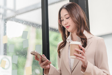 Professional woman engages with smartphone while enjoying coffee in modern workspace setting