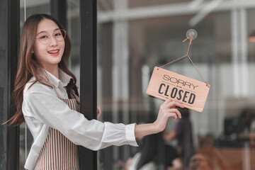 Smiling employee holds closed sign to inform customers of business hours