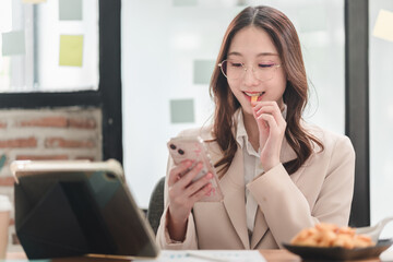 Young professional enjoys snack while engaging with smartphone in modern workspace setting