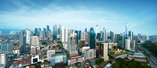 Panoramic view of Kuala Lumpur city skyline under a clear blue sky with highways and train tracks...