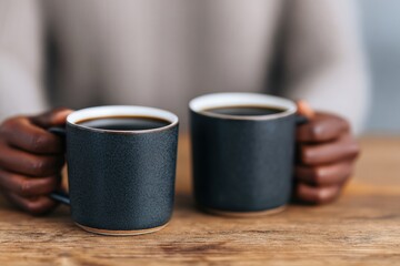 People are holding black coffee mugs on a wooden table, enjoying a moment of relaxation and conversation
