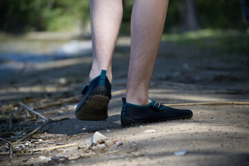 Person walking on a sandy path wearing minimal black shoes in nature.