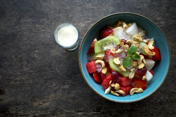 A bowl of colorful fruit salad with a combination of watermelon, strawberries, kiwi, grapes and garnished with mint leaves and cashew nuts