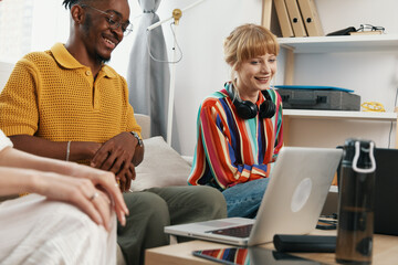 young adult coworkers socializing at workplace with laptop smiling woman and man collaborating in...