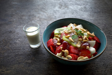 A bowl of colorful fruit salad with a combination of watermelon, strawberries, kiwi, grapes and garnished with mint leaves and cashew nuts