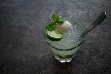 A glass of lemon water with ice garnished with lychee, sliced lemon and mint leaves