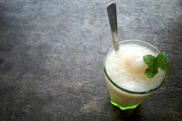 A glass of refreshing lychee drink with lime, mint leaves and ice, on wooden table