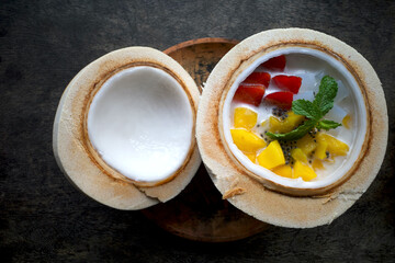 A mixed fruit salad, colorful dessert in half a fresh coconut, on a dark wooden table