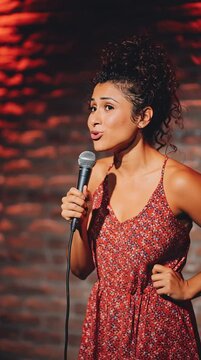 A Latina woman stand up comic performs a comedy routine and tells a joke on stage at a stand up comedy club